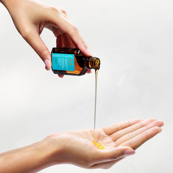 Een hand giet Moroccanoil Treatment olie in de andere hand.