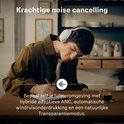 Jongeman met witte Sennheiser koptelefoon op, schrijft aan een tafel. Krachtige noise cancelling.