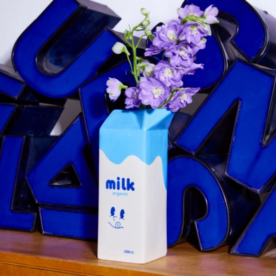 Witte vaas in de vorm van een melkpak met blauwe accenten. Tekst 'milk organic' en een gezichtje.