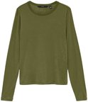 Model in een groen shirt met lange mouwen en een bruine broek, houdt een jas vast.