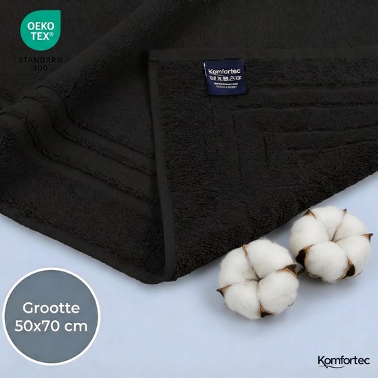 Detailopname van een zwarte badmat met OEKO-TEX STANDARD 100 label en "Komfortec" merklabel. Katoenplukken liggen ernaast. De tekst "Grootte 50x70 cm" is zichtbaar.