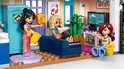 Drie LEGO Friends poppetjes in een woonkamer met een blauwe bank, televisie en groene planten.