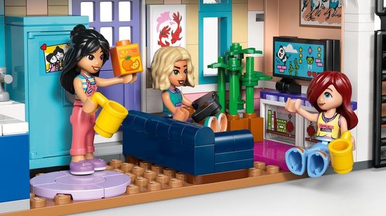 Drie LEGO Friends poppetjes in een woonkamer met een blauwe bank, televisie en groene planten.