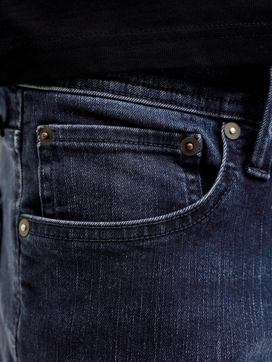 Detailopname van de donkerblauwe spijkerbroek met zakken en knopen.
