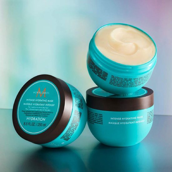 Drie potten Moroccanoil Intense Hydrating Mask op een kleurrijke achtergrond. Eén pot is open met crème.