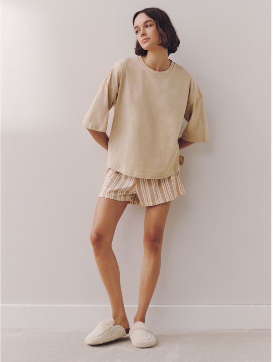 Model draagt een beige pyjamaset met effen top en gestreepte short.