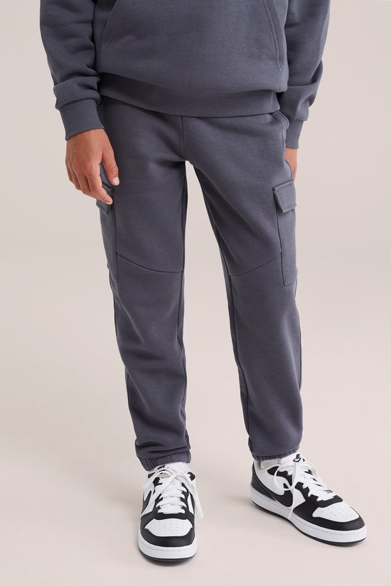 Jongen draagt donkergrijze cargobroek met witte sneakers.