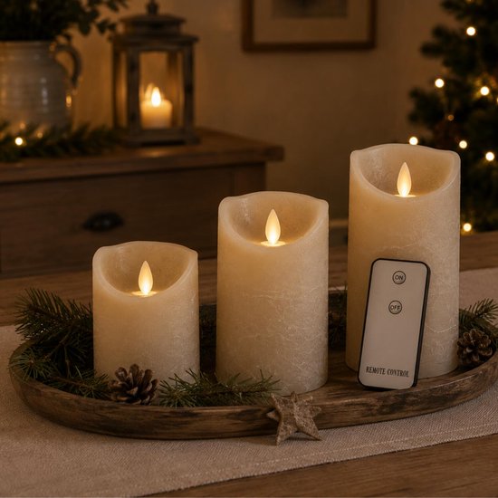 Drie taupekleurige LED stompkaarsen van Anna's Collection met afstandsbediening, decoratief op een schaal met dennentakken.