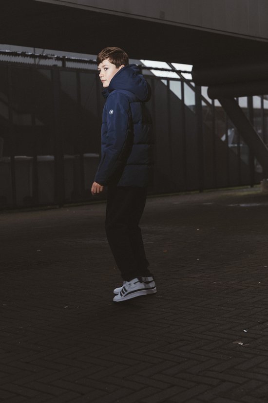 Jongen in een donkerblauwe pufferjas met capuchon en zwarte broek, draaiend weg van de camera.