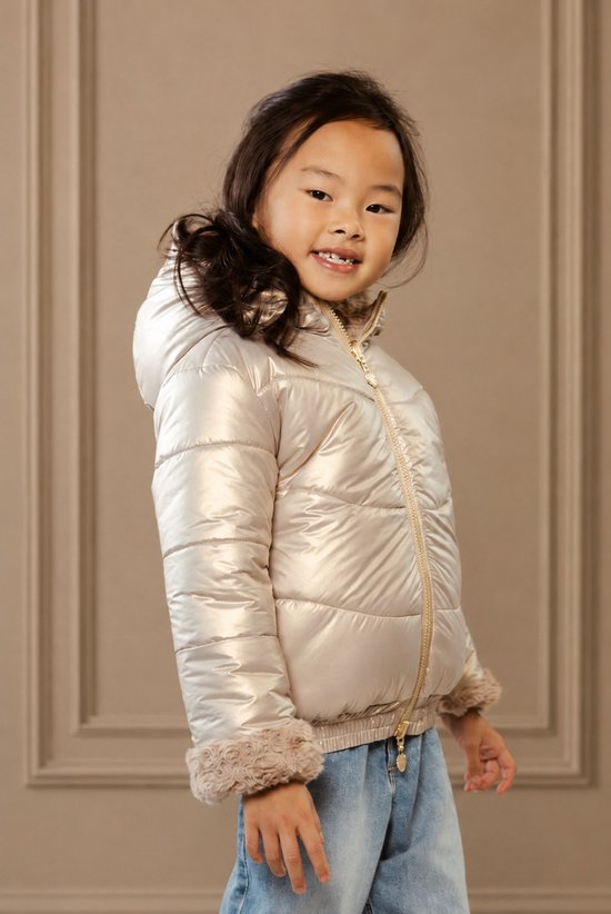 Meisje draagt goudkleurige winterjas met nepbont zomen, denim spijkerbroek.