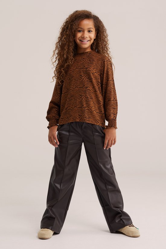 Meisje met lange krullen, draagt een bruine blouse met tijgerprint en zwarte broek.