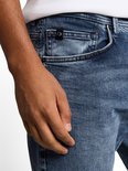 Detail van een blauwe denim jeans met stonewash-effect en het 'CI'-logo op de muntzak.