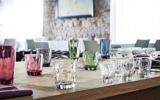Verres colorés et transparents à motif diamanté sur une table en bois.