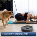 Zwarte ronde robotstofzuiger beweegt op houten vloer bij vrouw en hond, geschikt voor dierenharen.