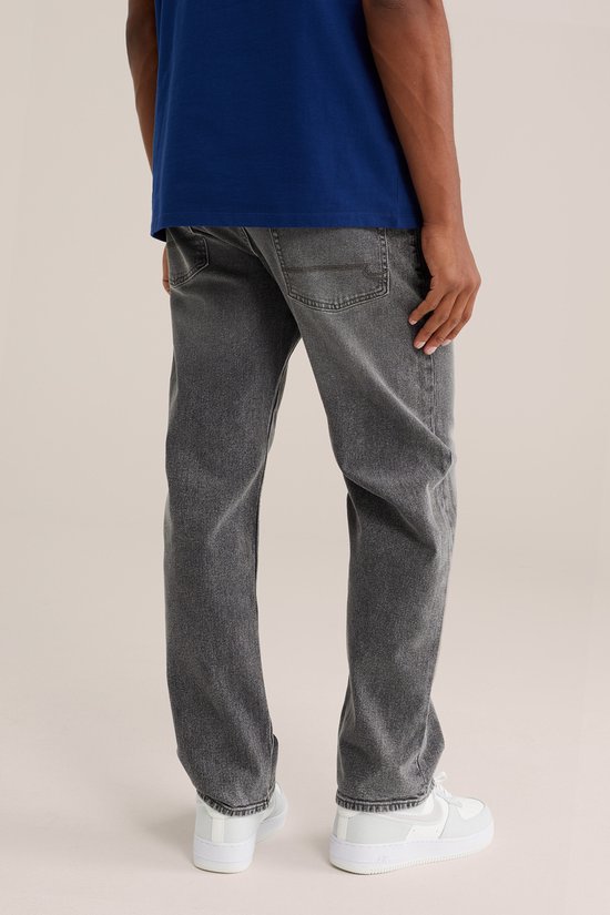 Model draagt grijze jeans met een relaxed fit, met de rug naar de camera. Drie witte sneakers.
