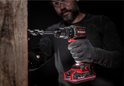 Een man met handschoenen boort in een houten plank met een rode en zwarte Einhell accuboormachine.