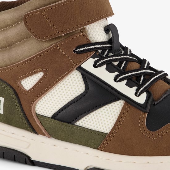 Close-up van een hoge sneaker met bruine, groene en zwarte vlakken. Witte mesh details en zwart-witte veters.