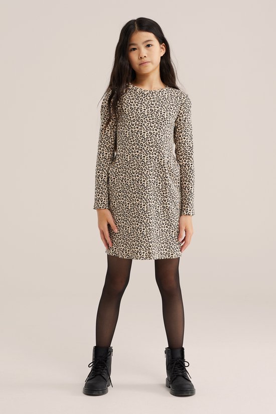 Meisje in een beige jurk met panterprint, zwarte panty en laarsjes.