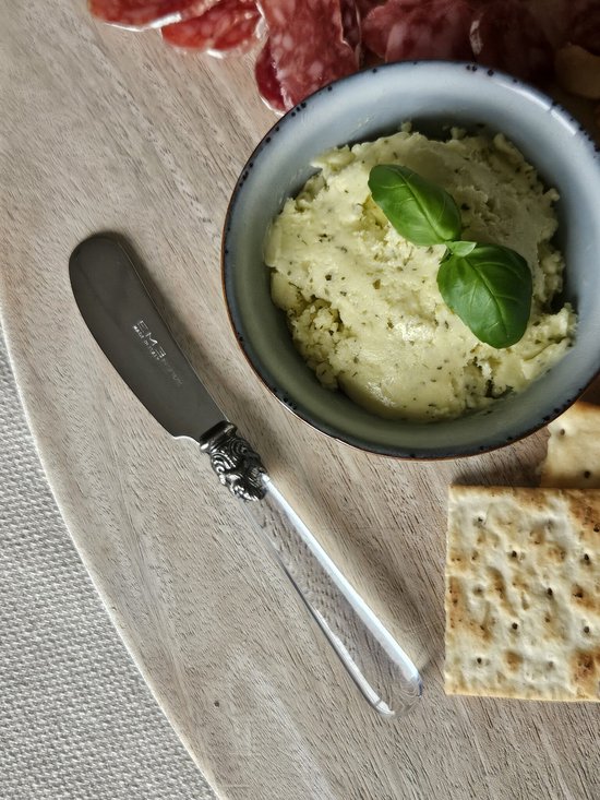 Boter mes met transparant handvat op een houten plank bij een kom met boter, crackers en vleeswaren.