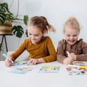 Twee lachende kinderen, een meisje en een jongen, met stempelstiften en Bluey kaarten.