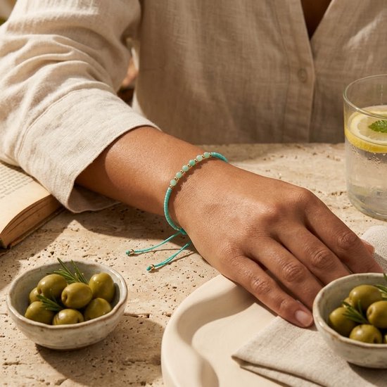 Turquoise koord armband met mintgroene kralen en gouden accenten, gedragen om een pols.