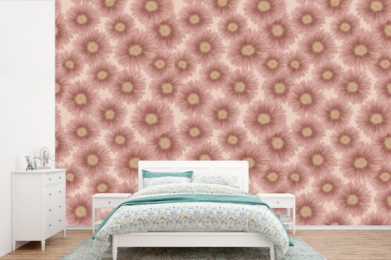 Roze behang met een repetitief patroon van roze gerbera's, boven een wit bed in een slaapkamer.