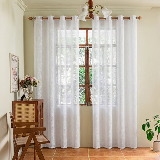 Twee zuiver witte inbetween gordijnen met ringen hangen voor een raam met houten kozijn. De stof heeft een subtiel geweven patroon.