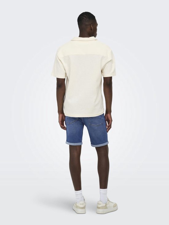 Man met korte mouwen, crèmekleurig hemd met open kraag. Blauwe jeans shorts, witte sokken en sneakers. Van achteren gezien.