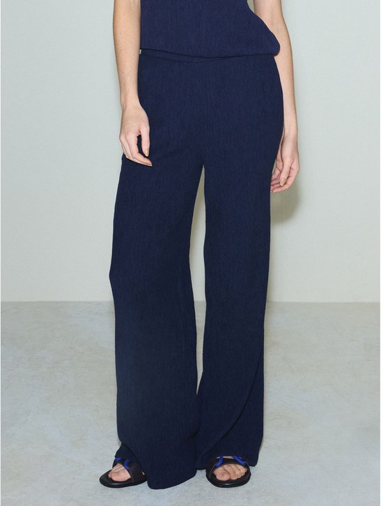 Marineblauwe broek met wijde pijpen en textuur, gedragen door een model.