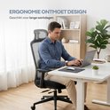 Man zit aan een bureau op een zwarte ergonomische bureaustoel en werkt op een laptop.