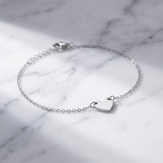 Zilverkleurige schakelarmband met een klein hartje op een marmeren ondergrond.
