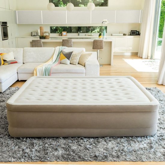 Un matelas pneumatique Intex de couleur crème dans un salon lumineux avec un grand canapé et un tapis gris.
