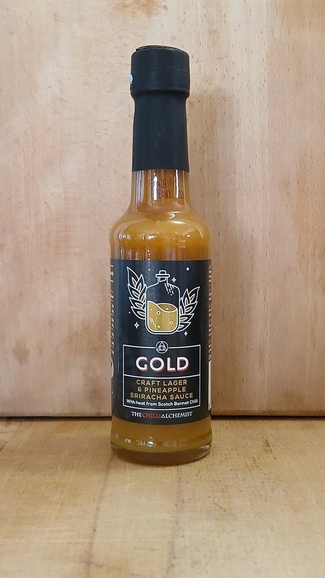 Fles "Gold" Craft Lager & Pineapple Sriracha Saus van The Chilli Alchemist met zwarte dop en label met een fles en bladmotief.