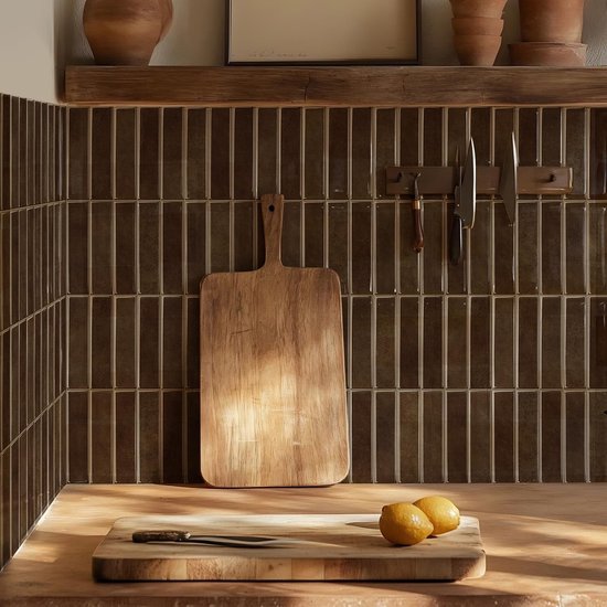 Een keukenachterwand met donkerbruine, rechthoekige tegels, met een houten snijplank en twee citroenen op het aanrecht.