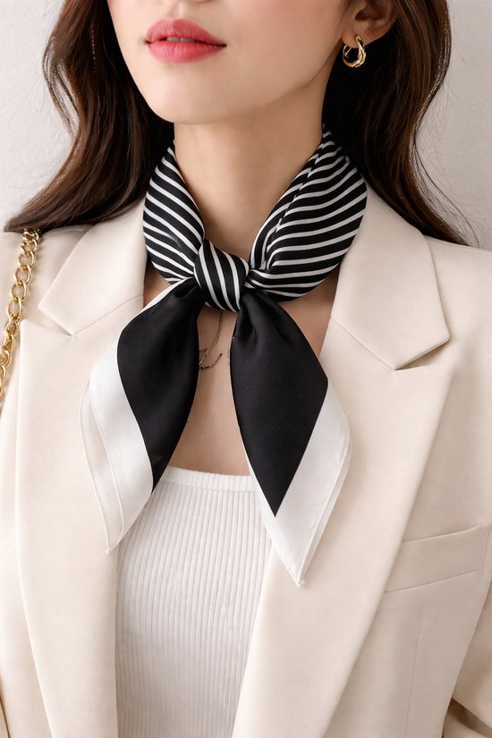 Model draagt een zwart-wit gestreepte vierkante sjaal met witte randen, geknoopt rond de nek, over een beige blazer.