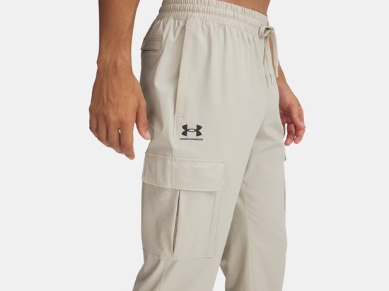 Man in beige cargobroek met cargo zakken, koord in de taille en Under Armour logo.