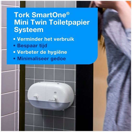 Witte Tork SmartOne Mini Twin Toiletpapier Dispenser aan een grijs betegelde muur.