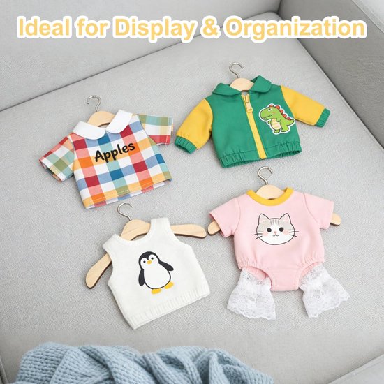 Vier poppenkledingstukken: een geruite blouse met 'Apples', een groen-gele jas met dinosaurusprint, een wit vest met pinguïn, en een roze romper met kattenprint.