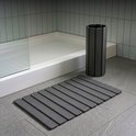 Een opgerolde donkergrijze badmat en een uitgerolde donkergrijze badmat naast een douche.
