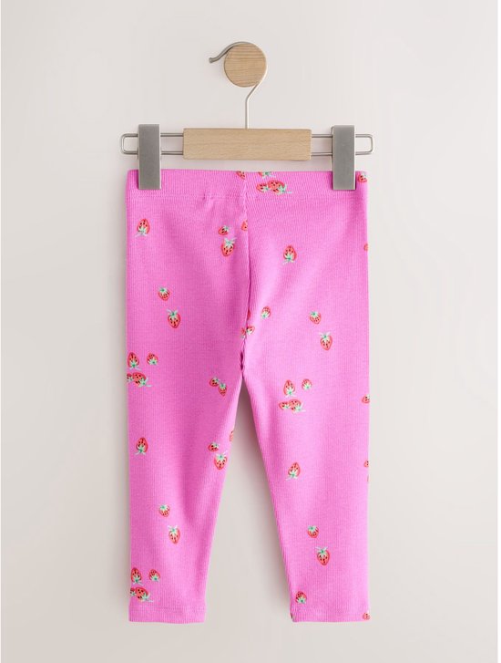 Roze, geribbelde legging met aardbeiprint, hangend aan een houten kleerhanger.