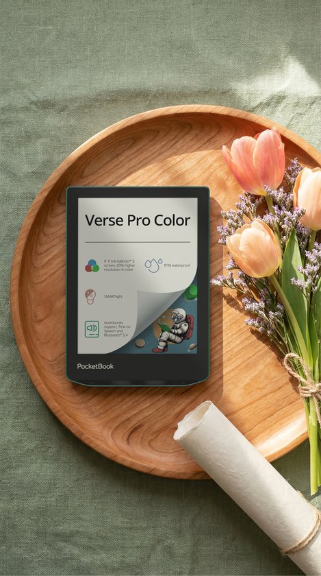 PocketBook Verse Pro Color op een houten schaal met bloemen, met zicht op de specificaties: 6" E Ink Kaleido 3 scherm, IPX8 waterdicht, SMARTlight, audioboeken.