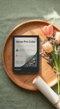 PocketBook Verse Pro Color op een houten schaal met bloemen, met zicht op de specificaties: 6" E Ink Kaleido 3 scherm, IPX8 waterdicht, SMARTlight, audioboeken.