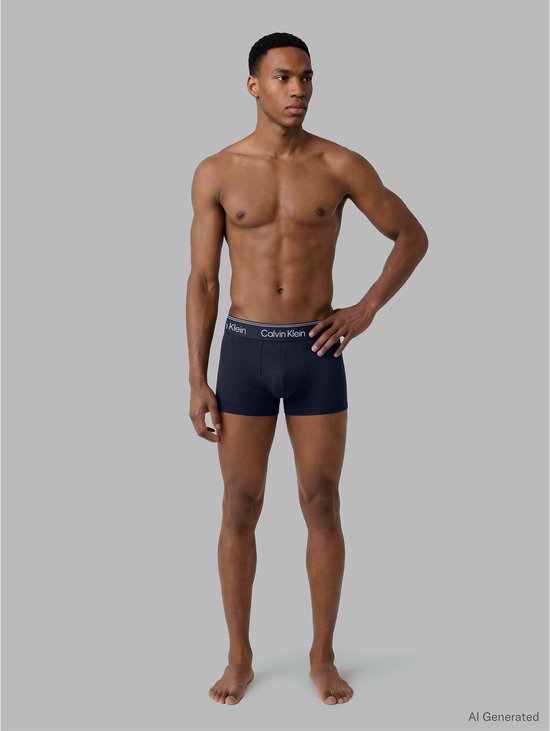 Man met navy Calvin Klein trunks, staand met de hand op de heup.