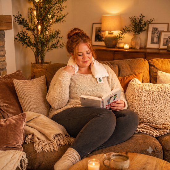 Vrouw met nek warmtekussen leest boek. Zachte beige kleur.