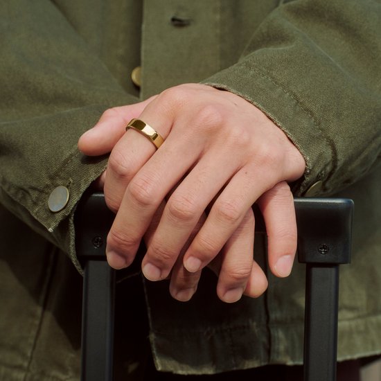 Handen met een gouden Oura Ring 5 om de vinger, dragend een groene jas.
