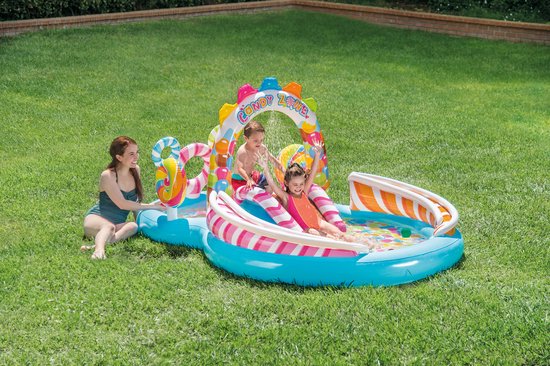 Een gezin geniet van het 'Candy Zone' speelbad met glijbaan in de tuin, met twee kinderen op de glijbaan en een vrouw zittend ernaast.