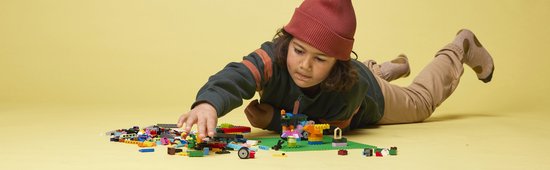 Kinderhanden bouwen met kleurrijke LEGO stenen op een groene bouwplaat.