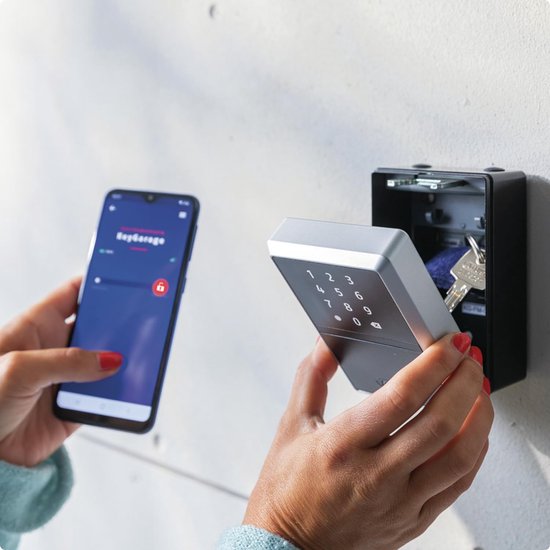 Handen gebruiken smartphone en ABUS sleutelkluis met cijfertoetsenbord.