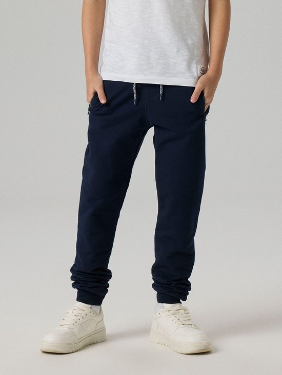 Jongen in donkerblauwe joggingbroek met trekkoord en ritszakken.