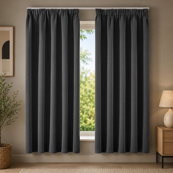 Donkergrijze verduisterende gordijnen hangen voor een raam in een woonkamer, met een lamp en plant ernaast.